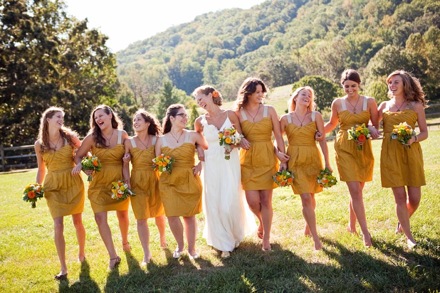Bridesmaids in matching mustard golden yellow knee-length A-line dresses walking through grass with bouquets