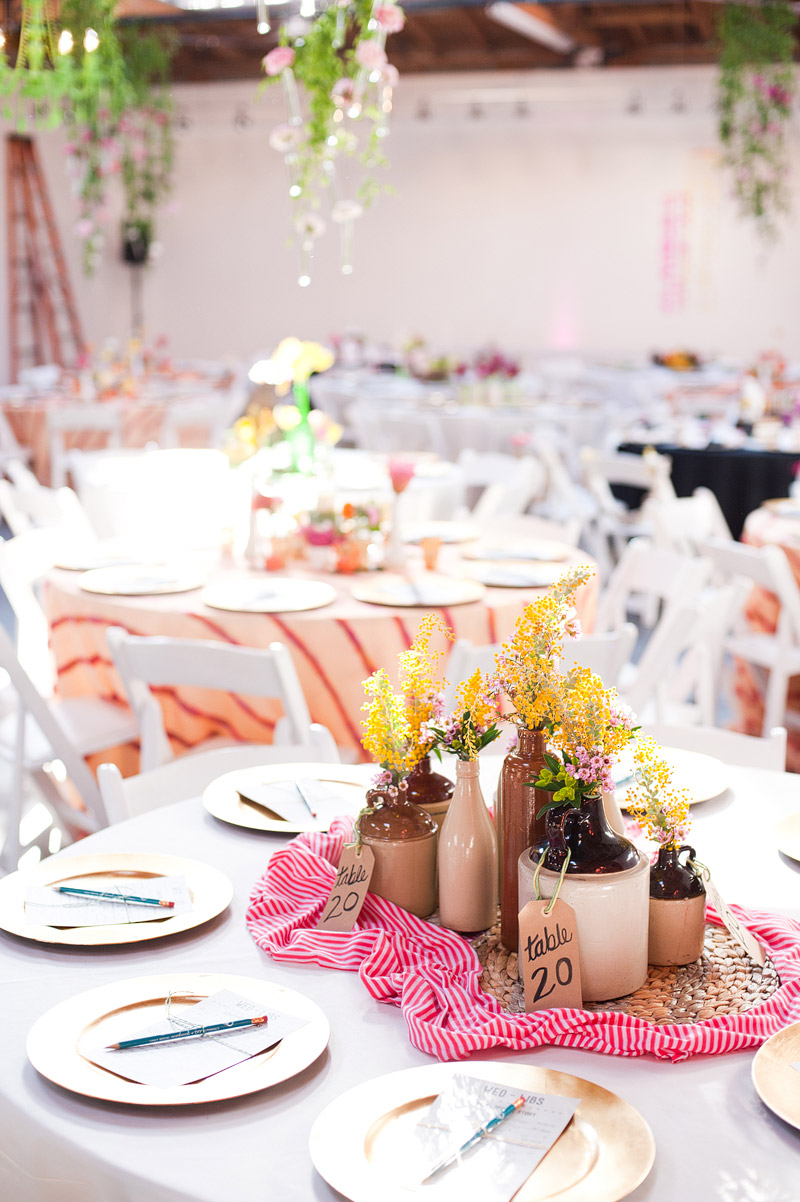 Clustered tin can bud vases with yellow wildflowers arranged on a table with gingham runner and handmade wood-burned table number