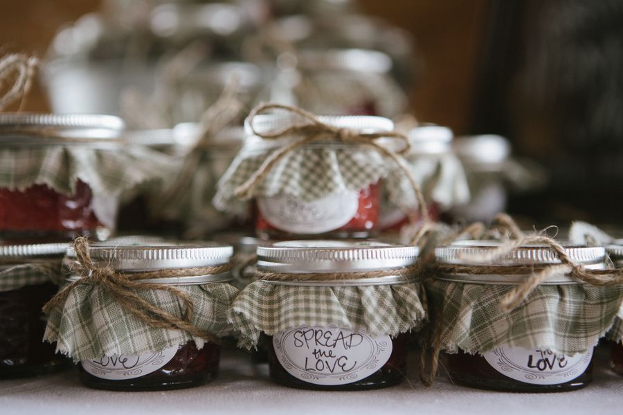 Rows of mini jam jars with green gingham fabric tops, jute twine bows, and 'Spread the Love' circular labels in red berry and dark blackberry varieties
