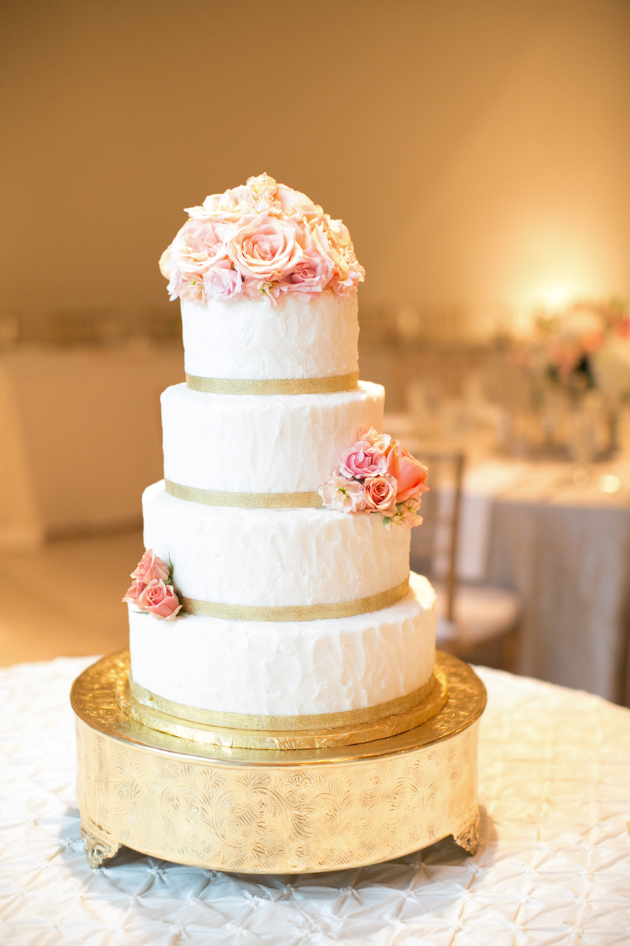Multi-tier wedding cake on a round ornate gold cake stand with small decorative feet
