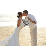 bride and groom kissing holding a thank you sign on the beach