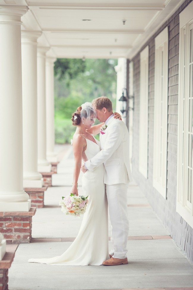 Bride in sleeveless V-neck ivory satin sheath dress with groom on columned porch