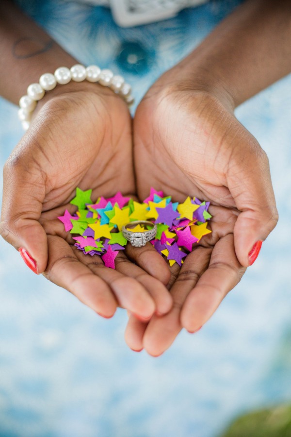 Cupped hands holding a halo diamond ring nestled in bright multicolored foam star confetti