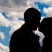 bride and groom kissing and shadowed out with blue sky and clouds in background
