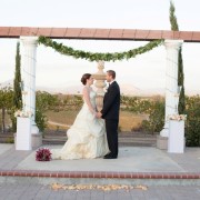 bride and groom standing at altar at Mount Palomar Winery with peach rose petals and fountain