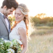 bride and groom standing together in field.  Bride holding wild flower bouquet and braid in her hair.