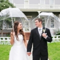 17 Bride and groom standing in front of PATRICK RANCH MUSEUM holding clear umbrella