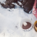 2 mugs sitting in the snow with hot chocolate inside and floating marshmellow