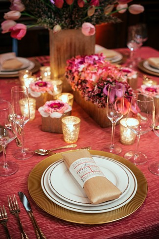 Romantic pink and gold wedding place setting with a gold charger, kraft menu napkin, pink tulip centerpiece, and glowing mercury votives