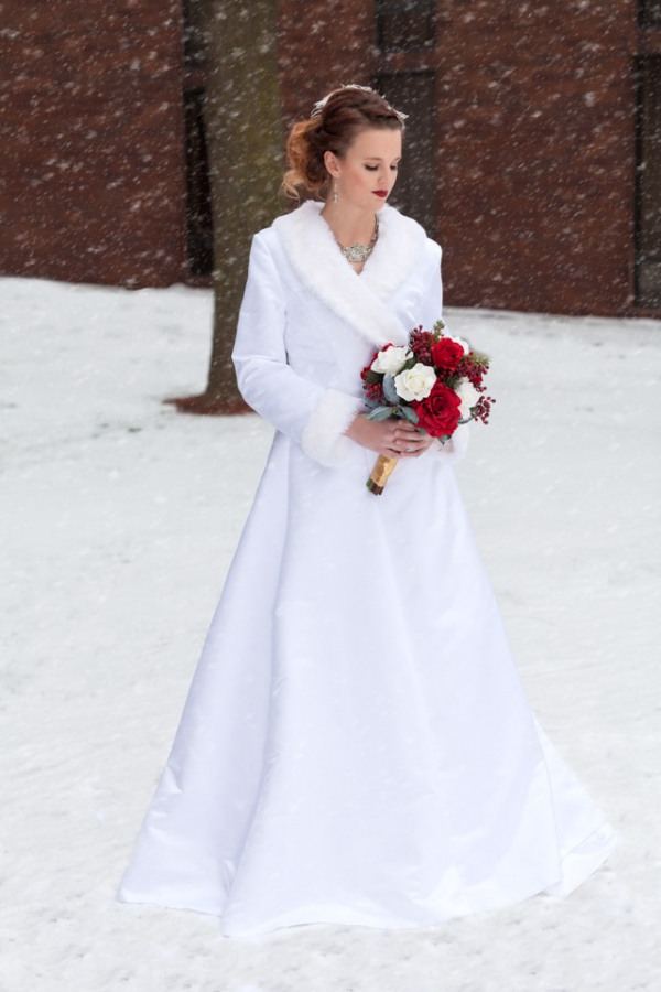 Bride in elegant white satin coat dress with fur-trimmed collar and cuffs in falling snow