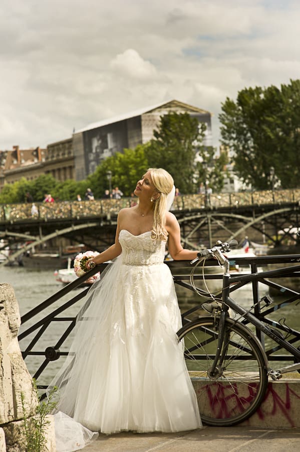 Blonde bride in sweetheart tulle ball gown with lace appliques posing along the Seine River in Paris with bridge in background