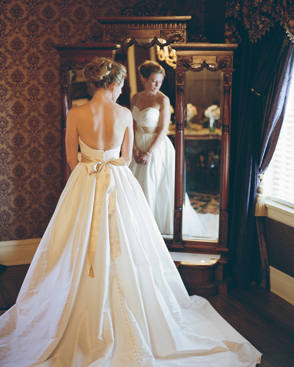 Back view of bride in strapless satin A-line wedding gown with gold sash bow at waist, reflected in antique mirror at Tate House Mansion