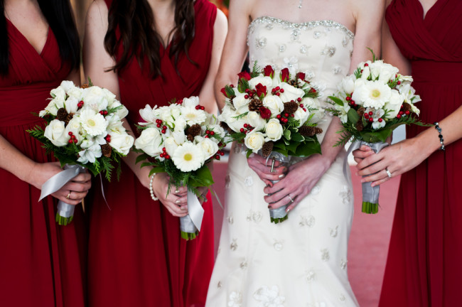 Bride standing with bridesmaids in red dresses holding white rose bouquet 