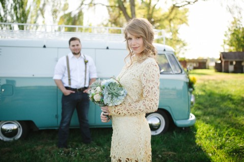 Bride in cream lace long-sleeve mini dress holding succulent bouquet with vintage turquoise VW bus in background