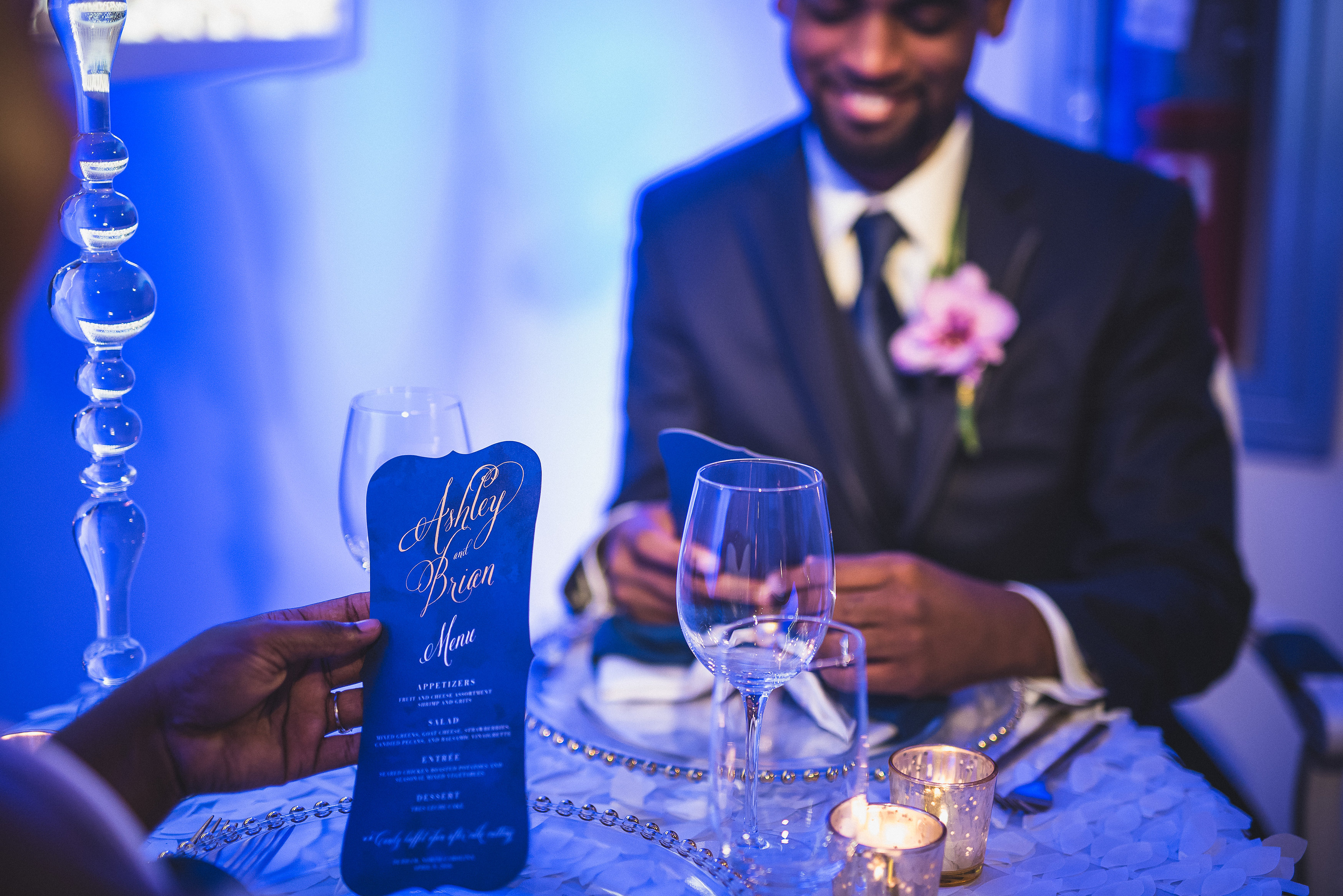 Hand holding a blue menu card reading Ashley and Brian Menu with appetizers, salad, entree, and dessert