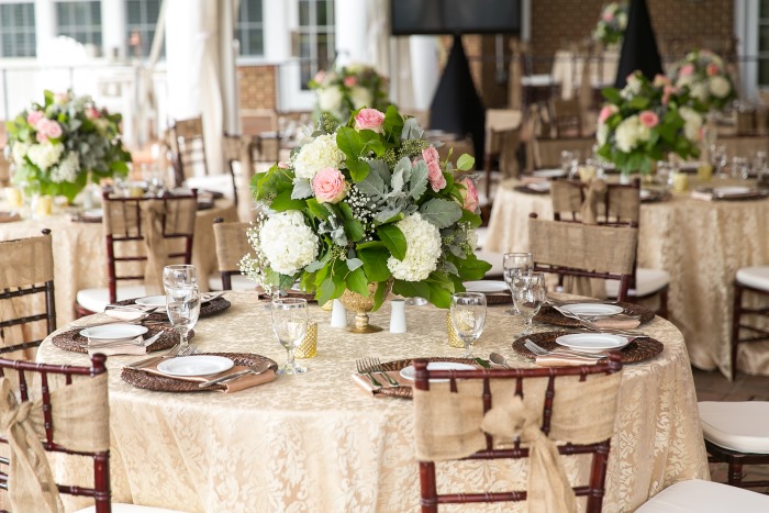 Low gold mercury glass vase with white hydrangea and pink roses on a round table with gold damask linen and rattan chargers