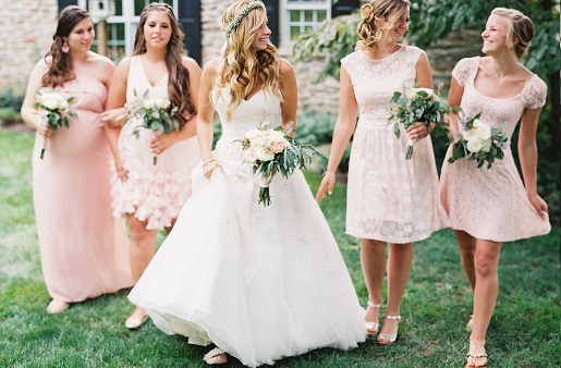 Bride with baby's breath flower crown walking with bridesmaids in mismatched pink Modcloth dresses holding white and greenery bouquets