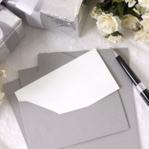 Writing paper or wedding invitation with envelope laid on bridal lace with several wedding gifts