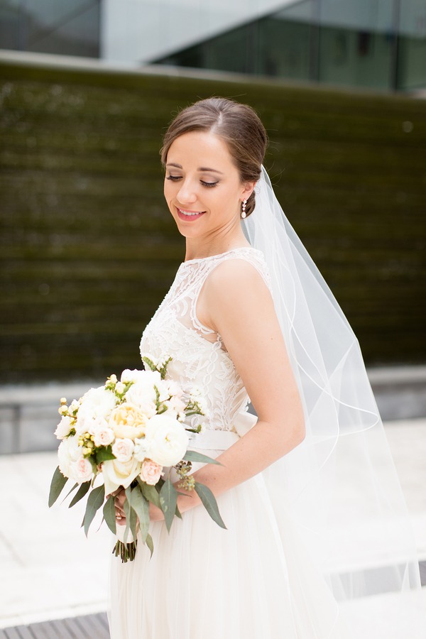Bride in white a-line wedding dress with high neckline, lace bodice, and chiffon skirt holding bouquet