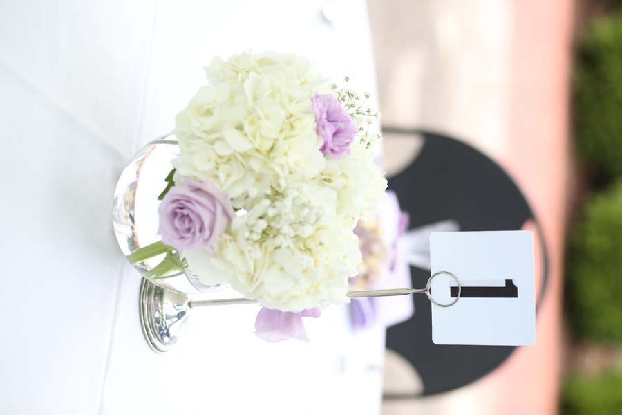 Low clear bubble bowl centerpiece with white hydrangea and lavender roses on a white round table outdoors