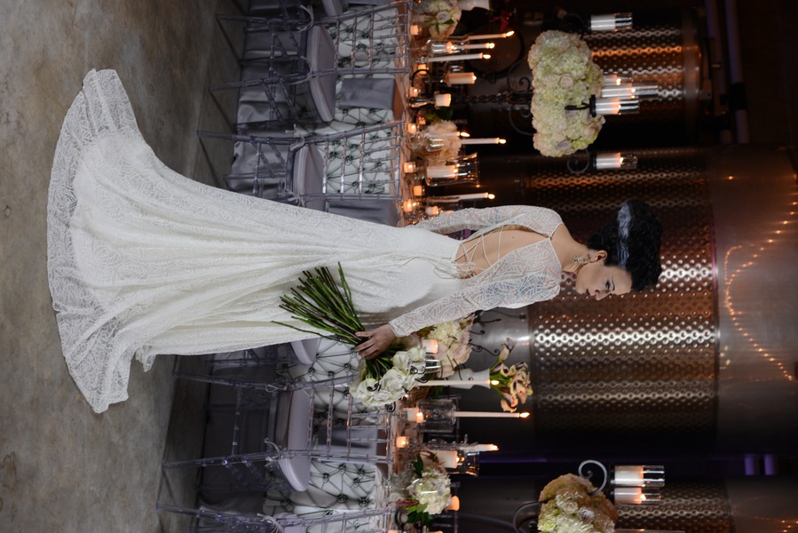 Bride in long-sleeve lace gown with dramatic lace-up corset back and full skirt in moody industrial setting