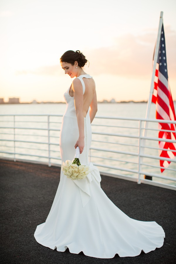 Bride in sleek crepe mermaid gown with open back and bow detail on waterside deck at sunset