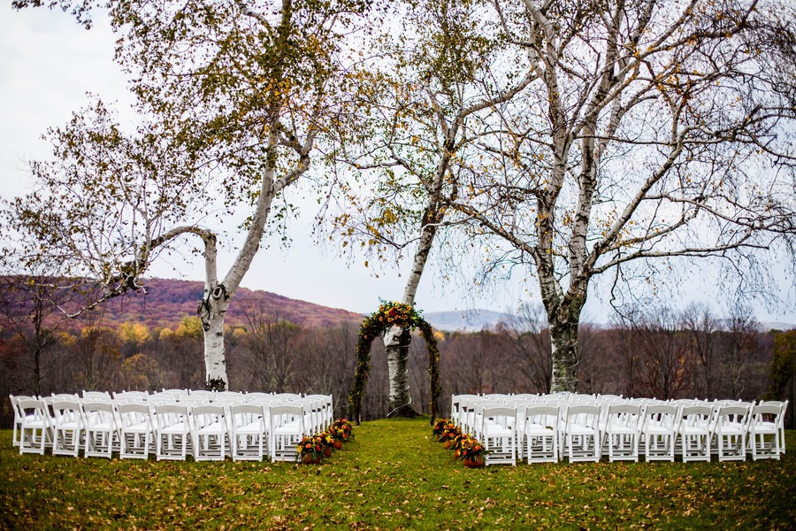 Round wedding arch with orange and yellow autumn flowers set between two large white birch trees on a hilltop