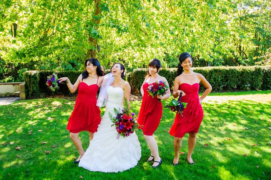 Three bridesmaids in bright true red knee-length strapless dresses posing playfully on a green lawn