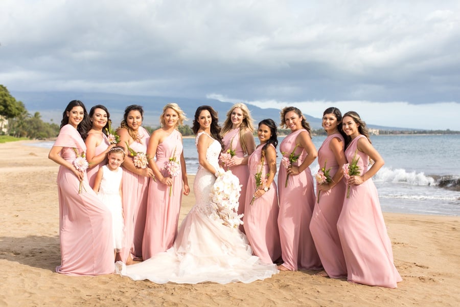 Bridesmaids in mismatched dusty rose and blush chiffon gowns on a Maui beach with the bride