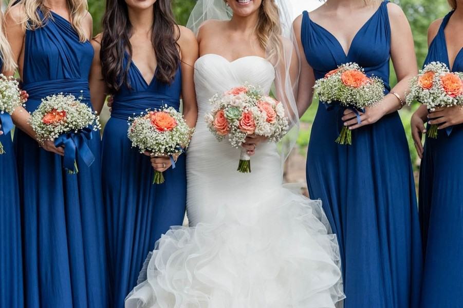Bride in mermaid gown with bridesmaids in navy blue dresses holding coral rose and baby's breath bouquets