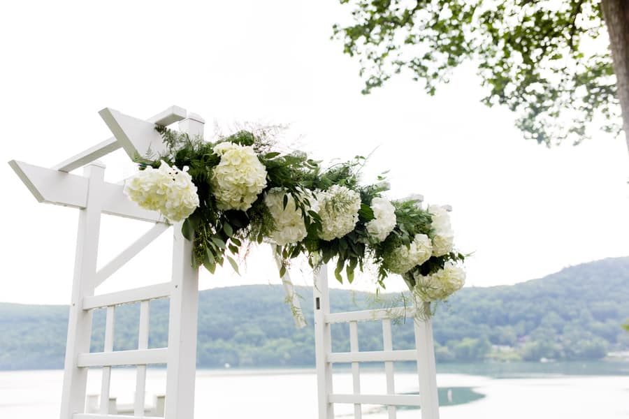 White wedding arbor decorated with white hydrangea and greenery garland overlooking lake and mountains