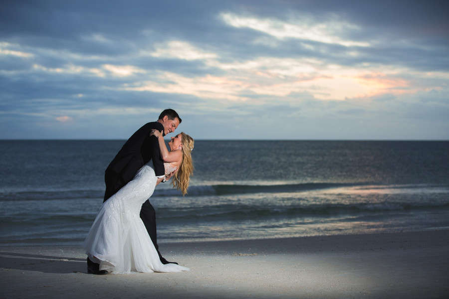 Dramatic sunset silhouette of groom dipping bride on beach