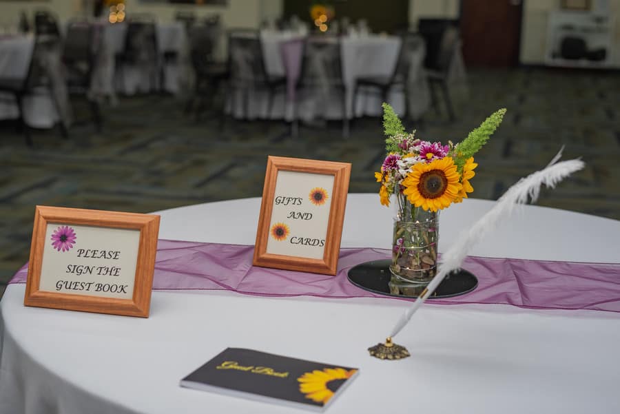 White round table with sheer purple organza runner, wood framed signs, and sunflowers