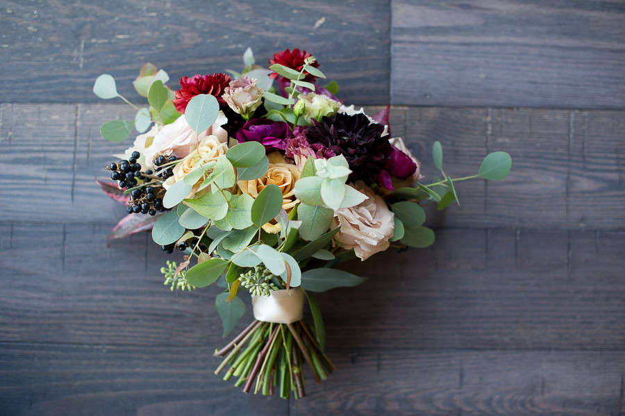 Rich bouquet with burgundy dahlias, peach roses, plum ranunculus, eucalyptus and navy berries against gray wood