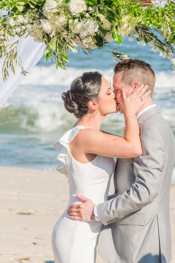 Bride and groom kissing under floral archway on Long Beach Island
