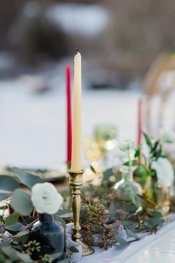 Table runner with eucalyptus greenery, brass candlesticks with red and ivory taper candles, and geometric accents