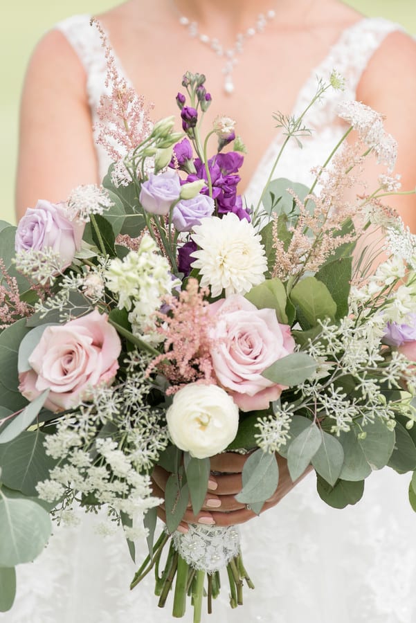 Bride holding lush garden-style bouquet with lavender roses, pink astilbe, purple stock, white dahlia, and baby's breath