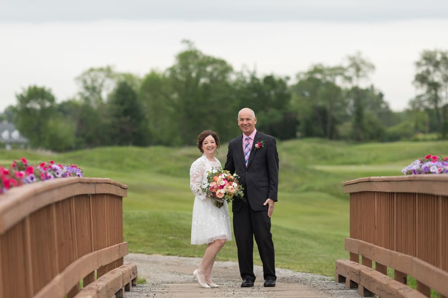Couple on wooden bridge with flower boxes, bride in white lace tea-length dress with long sleeves