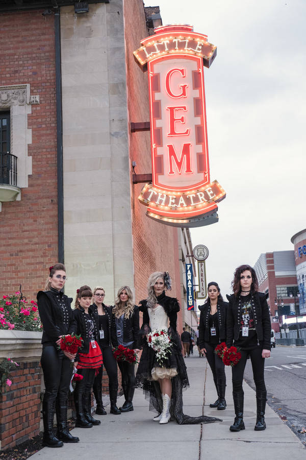 Bride in white corset bodice with black lace and tulle hi-lo skirt with bridesmaids in black military jackets outside theatre