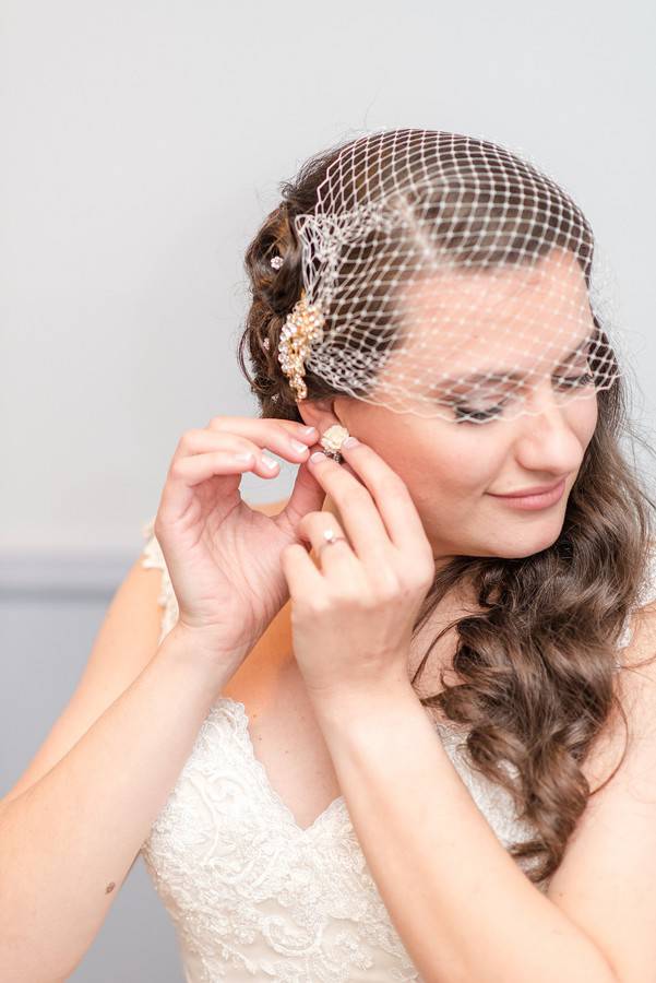 bride-getting-ready-putting-on-earrings-bird-cage-veil
