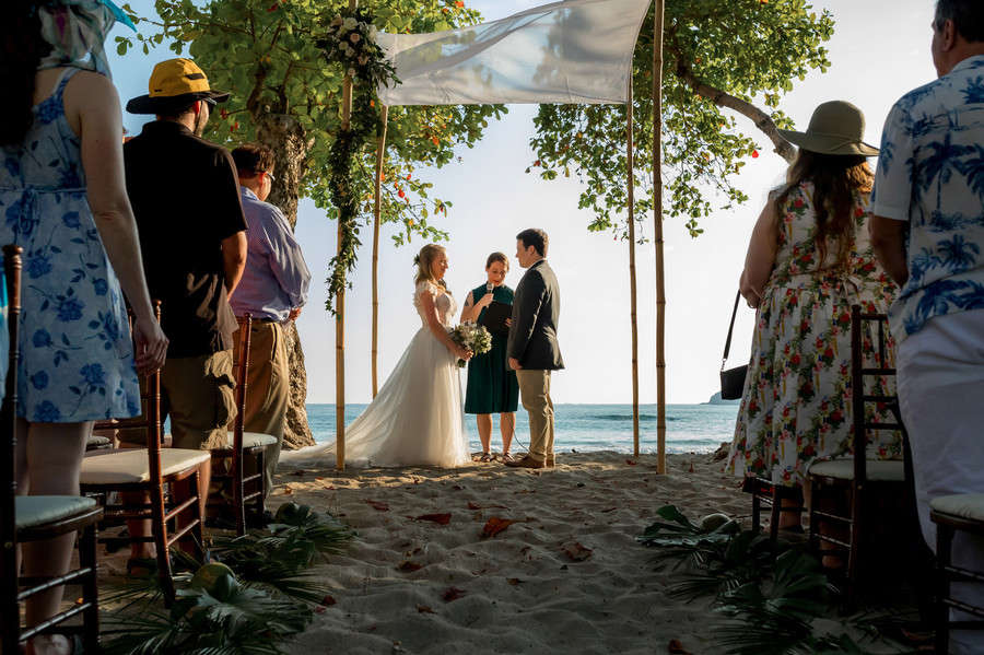 Bride and groom ceremony on beach with ocean backdrop exchanging vows