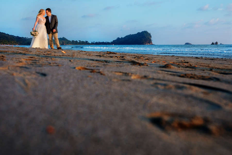 Bride and groom walking on beach with blue ocean, low angle shot