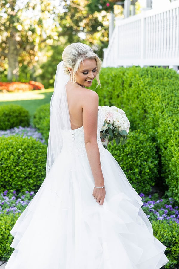 Bride in strapless ruffled ballgown with low back holding white rose bouquet in garden setting