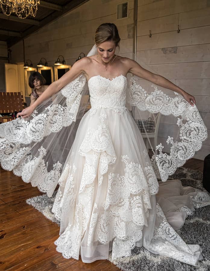 Bride in strapless sweetheart ball gown with tiered scalloped lace skirt spreading matching scalloped lace veil