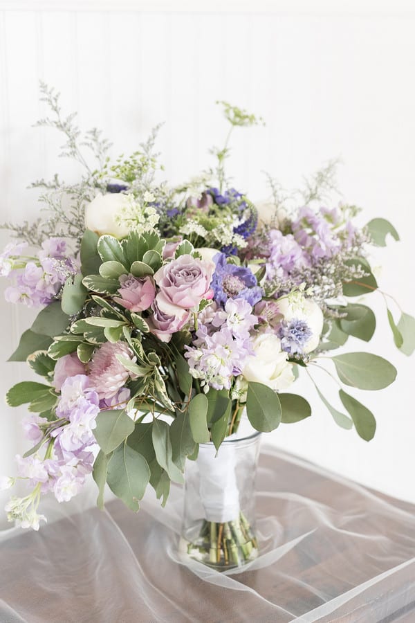 Lavender wedding bouquet with purple stock, mauve roses, blue scabiosa, white peonies, succulents, and silver dollar eucalyptus wrapped with white ribbon