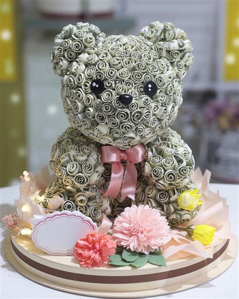 Teddy bear sculpture made of small white roses, with a pink ribbon bow, surrounded by artificial flowers and decorative lights on a round base—perfect for creative money gifts or unique cash gift ideas.