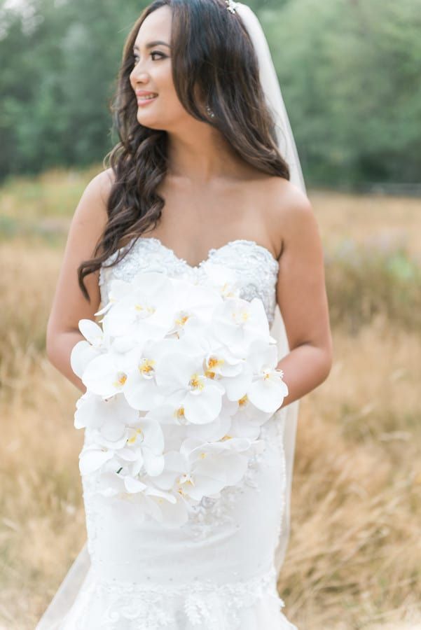 Bride holding cascading white phalaenopsis orchid bouquet in outdoor golden field setting wearing strapless sweetheart gown
