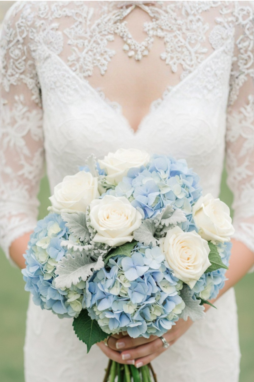 Bride in long-sleeve lace gown holding blue hydrangea bouquet with white roses and dusty miller accents