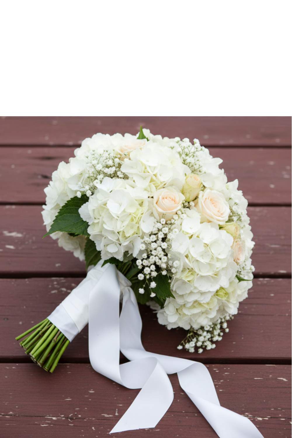 White hydrangea bouquet with blush roses and baby's breath tied with white satin ribbon on rustic wood surface