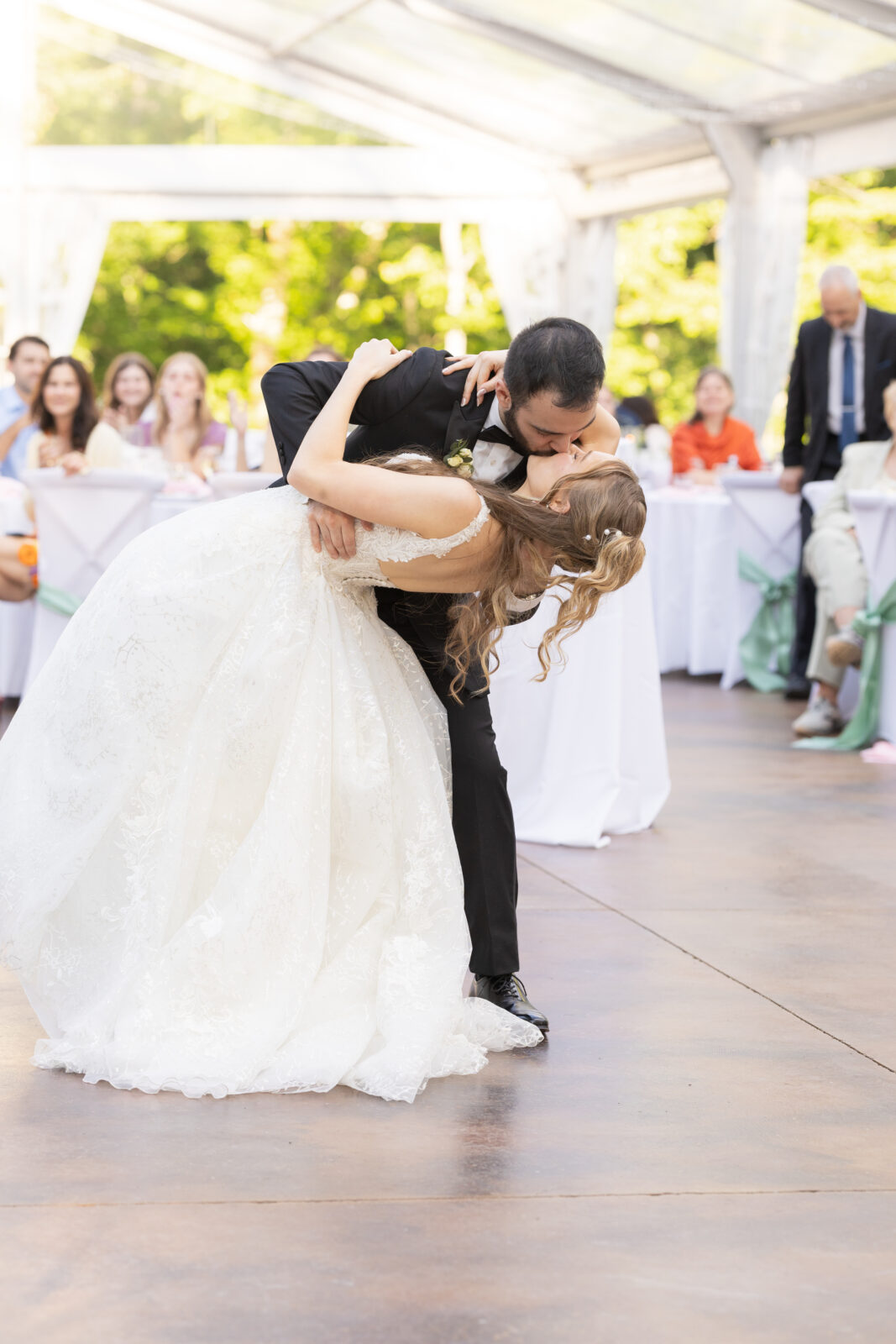 A bride and groom share a dip kiss on the dance floor at their wedding reception, with guests seated and watching in the background.